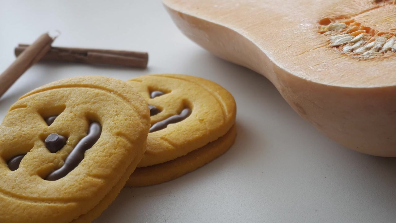 白い表面に置かれたカボチャの形をしたクッキー、シナモンスティック、そしてスライスされたスカッシュ。