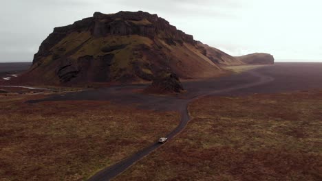 aerial 4k view of a dacia duster suv car driving on a gravel road on a black sand beach with a mountain background, iceland, europe, orbiting shot