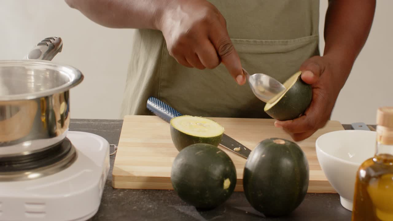 Man in green apron grabbing knife and spoon, cutting, scooping melon on cutting board for cooking