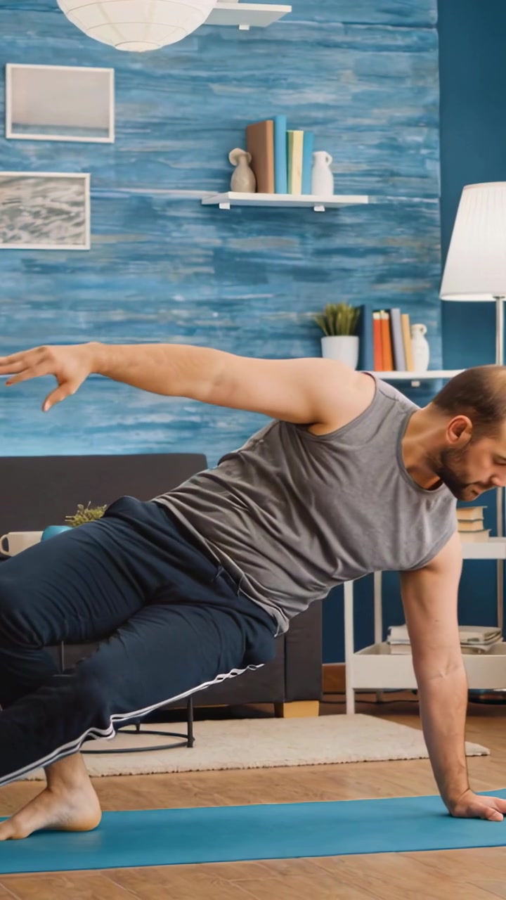 Vertical video: Starting on blue mat, gray-top man flowing sideplank-to-stand at home for balance
