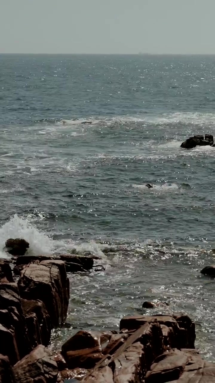 Onde marine che si muovono attraverso una costa rocciosa con schiuma e una superficie dell'acqua increspata.