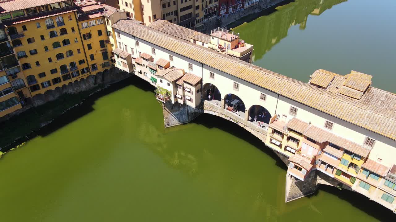 Cinematic aerial of iconic Ponte Vecchio bridge over green Arno river Florence