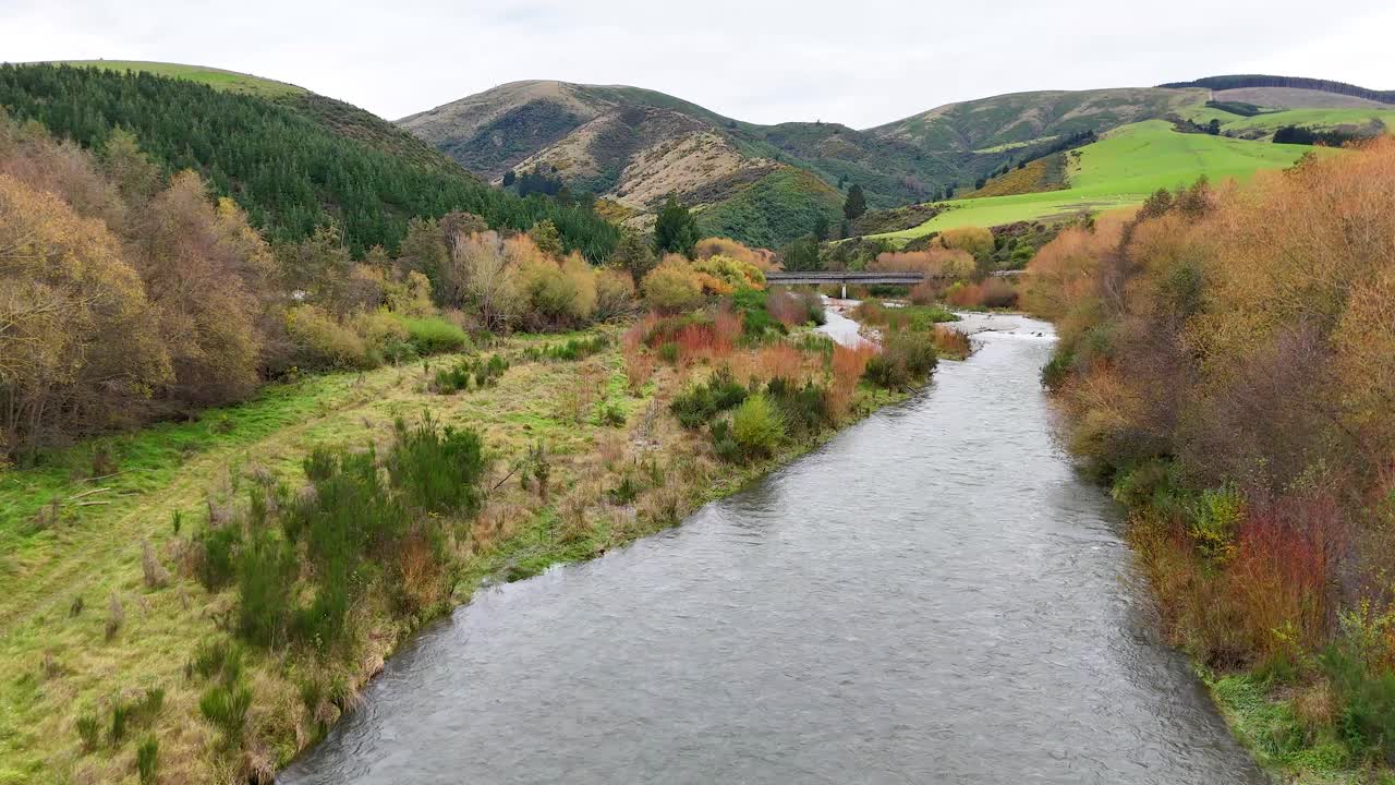 A tranquil river meanders through lush greenery and rolling hills under soft, natural lighting in Lake Tekapo, New Zealand