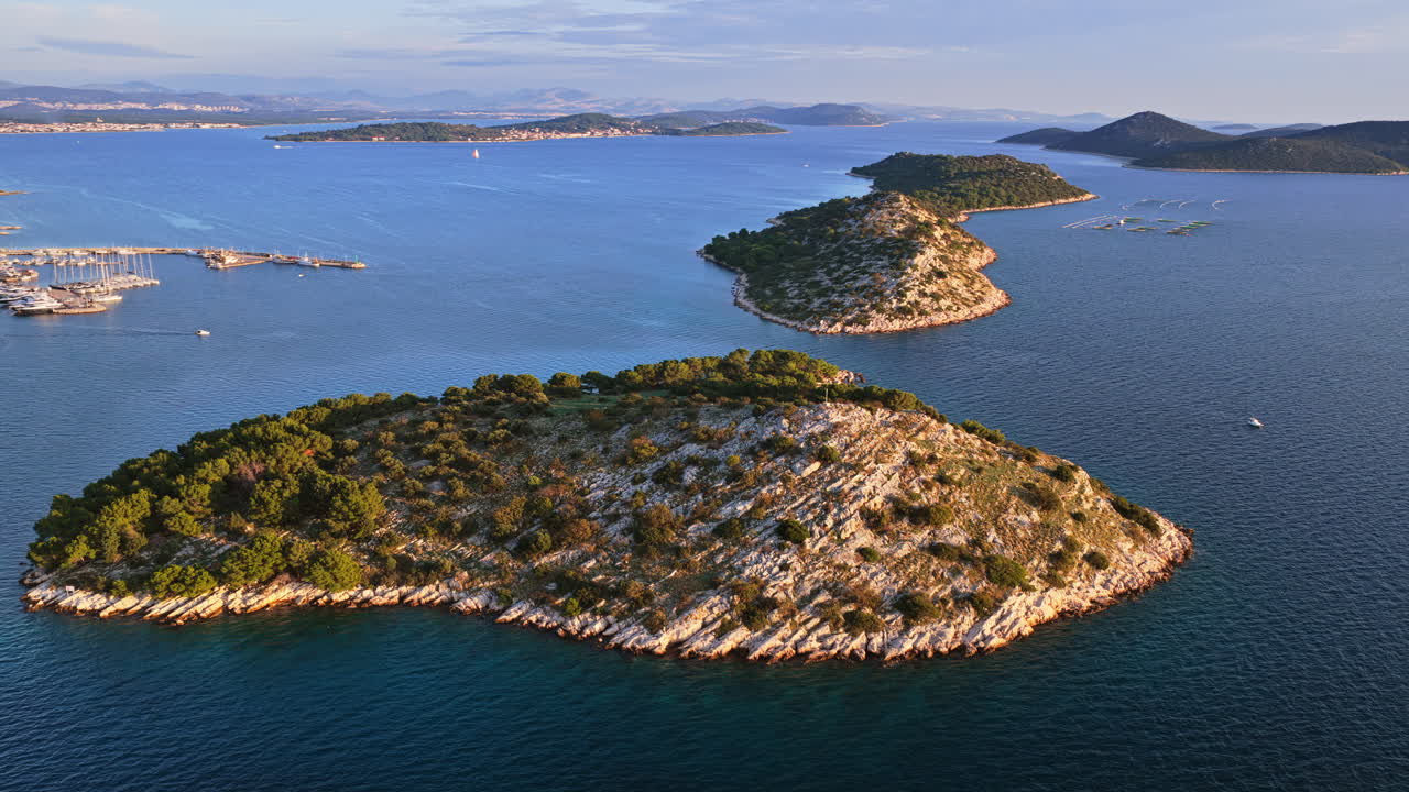 Aerial drone view of several rocky, pine covered islands stretching across the calm blue waters of Croatia near Tribunj