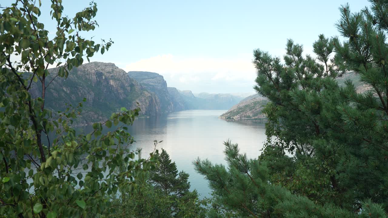 En lugn norsk fjord fångad vid soluppgången, med berg som ramar in de stilla vattnen. Frodig grönska ger liv åt det naturliga landskapet och skapar en fridfull atmosfär.