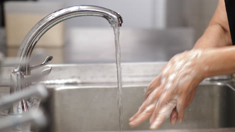 slow motion of asian woman chef washing hands in kitchen sink with foam and flow water from tap