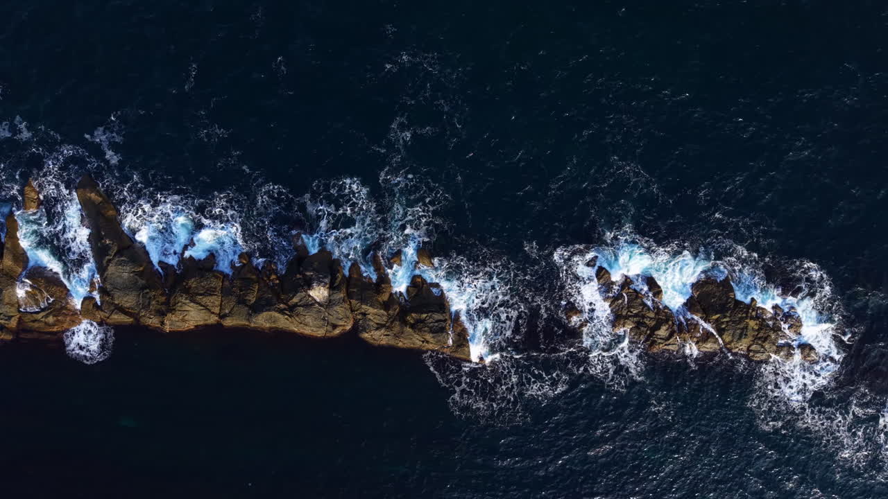 Waves crash against rugged rocks at the coastline during a serene sunset, creating a breathtaking natural spectacle full of movement and beauty