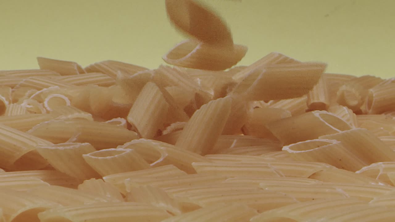 macro de plumas medio surcadas secas que caen o pasta mezze penne rigate sobre fondo amarillo