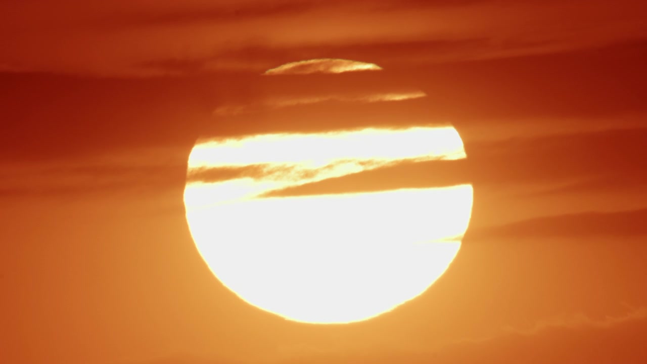 密集した都市のスカイラインの向こうに沈む黄金の夕日。中層の住宅ビルがシルエットになっている。