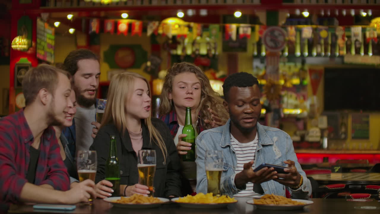 Gruppo di amici felici multirazziali che brindano con la birra in un bar o pub