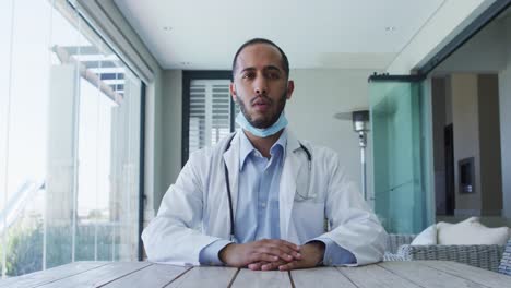 Mixed-race-male-doctor-wearing-face-mask-talking-during-video-call