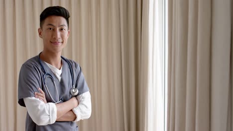 portrait of happy biracial male doctor against beige curtains with copy space, slow motion