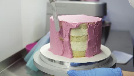 el proceso de decorar un pastel con una cubierta de crema púrpura. el confitero iguala la crema de galleta usando una espátula de pastelería