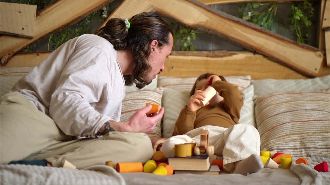 Father playing with his son with colourful, ecological wooden toys on the bed