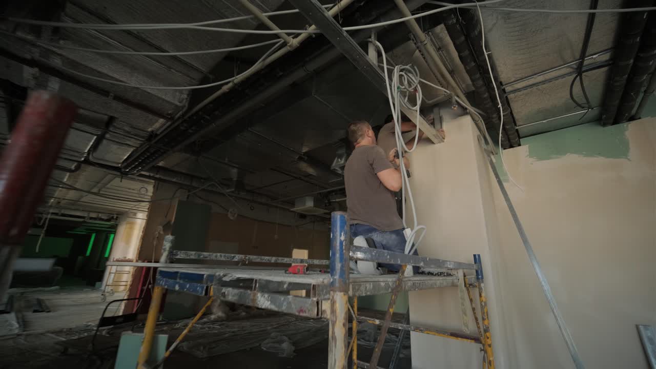 Construction worker assemble a suspended ceiling with drywall and fixing the drywall to the ceiling metal frame with screwdriver. Renovation, construction and do it yourself DIY concept.