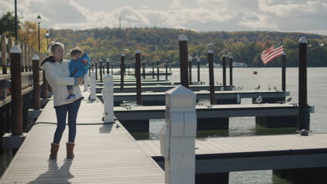 a woman with a child in her arms walks along the pier, in the distance the us flag