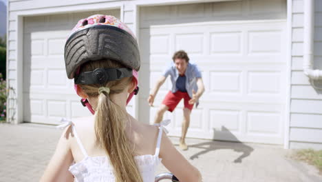 Vista-Trasera,-Niña,-Andar-En-Bicicleta,-Padre,-Enseñanza,-Hija,-Cómo-Andar-En-Bicicleta