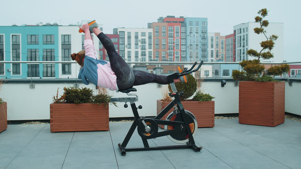 Athletic woman makes twine training routine on spinning stationary bike on house roof weight loss