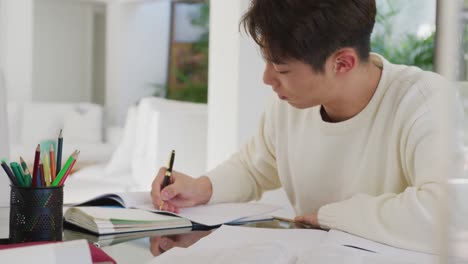 asian male teenager taking notes and sitting in living room