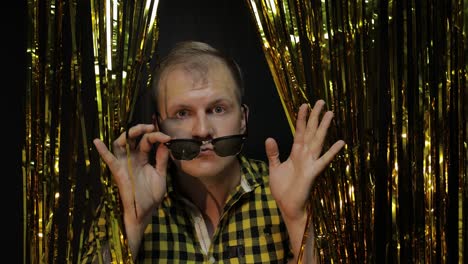 portrait of caucasian man posing on black background. gold shining foil strips. party, music, disco