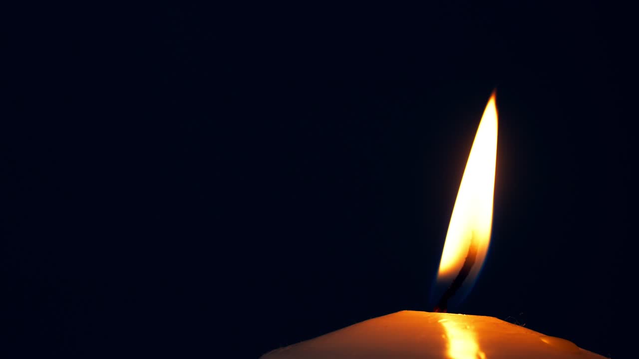 Una singola grande fiamma di candela gialla si accende e si spegne, isolata su sfondo nero