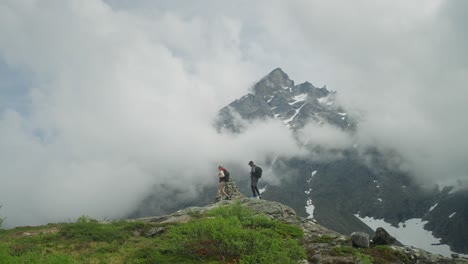 Two-hikers-stand-on-a-rocky-outcrop,-admiring-mist-covered-mountains-in-Norway