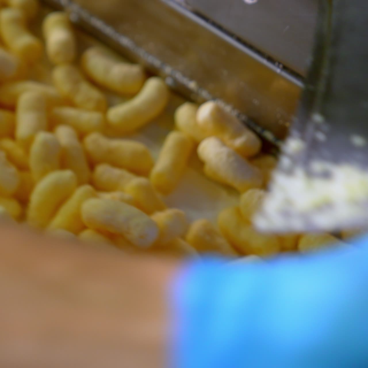 Light yellow crispy snacks falling on the conveyor belt. Corn sticks coated with sugar frosting close up