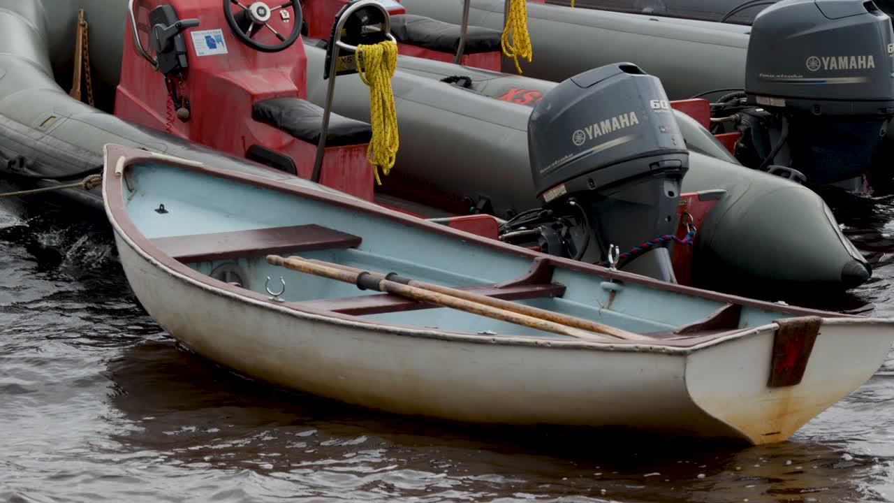 Stationary inflatable boats and rowboat with outboard motors, overcast daylight, slight camera pan, harbor setting