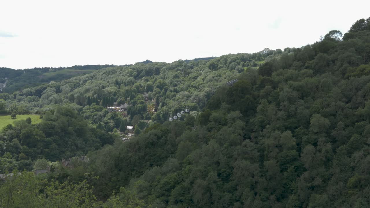 Cable cars moving slowly with green forest backdrop on overcast day