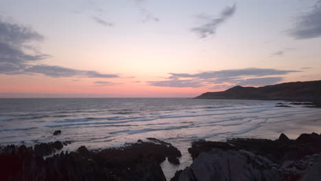 right to left pan of waves crashing against a sandy beach at dusk