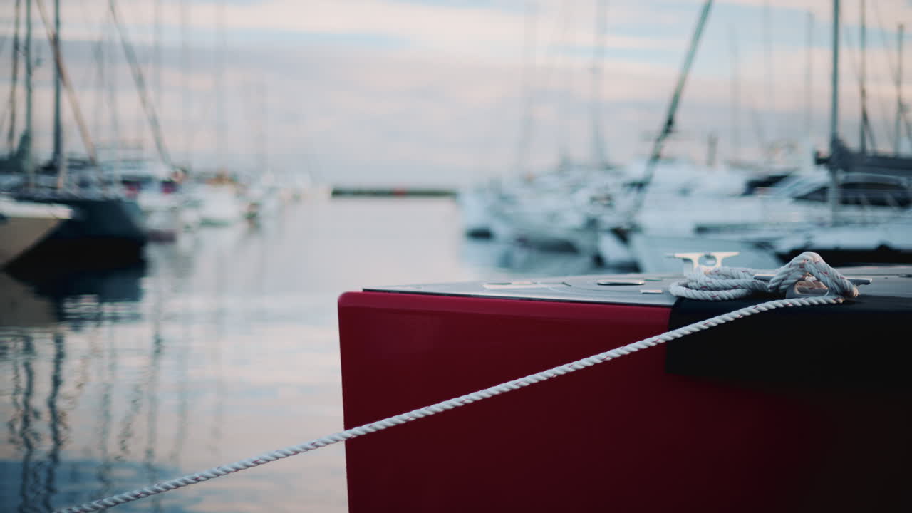 Peaceful marina view showing a red boat tied with white ropes, surrounded by yachts on calm water