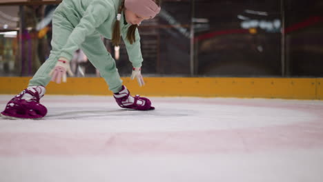 a close view of a child practicing skating on an ice rink, the child is wearing mint green pants and pink skates, bent down in concentration, working on balance and movement