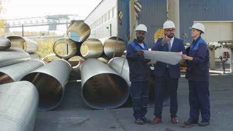 manufacturing engineer and workers looking at blueprints at plant