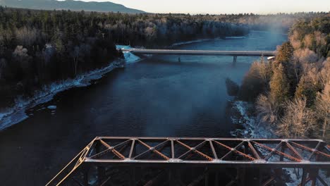 Imágenes-Aéreas-Que-Vuelan-Lentamente-Sobre-Un-Caballete-De-Ferrocarril-Y-Hacia-Un-Puente-Que-Cruza-Un-Río-De-Invierno-Al-Amanecer