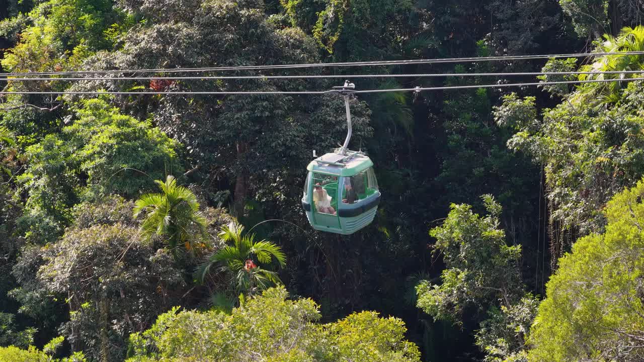 Aerial view of a cable car gliding over dense rainforest, showcasing vibrant greenery and serene movement