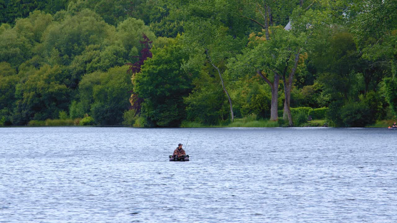 Distant View Of A Man Float Tube Fishing Over Tranquil Lake. Aerial Slow Motion Shot