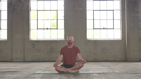 man in an industrial warehouse practicing yoga, the pose of meditation.