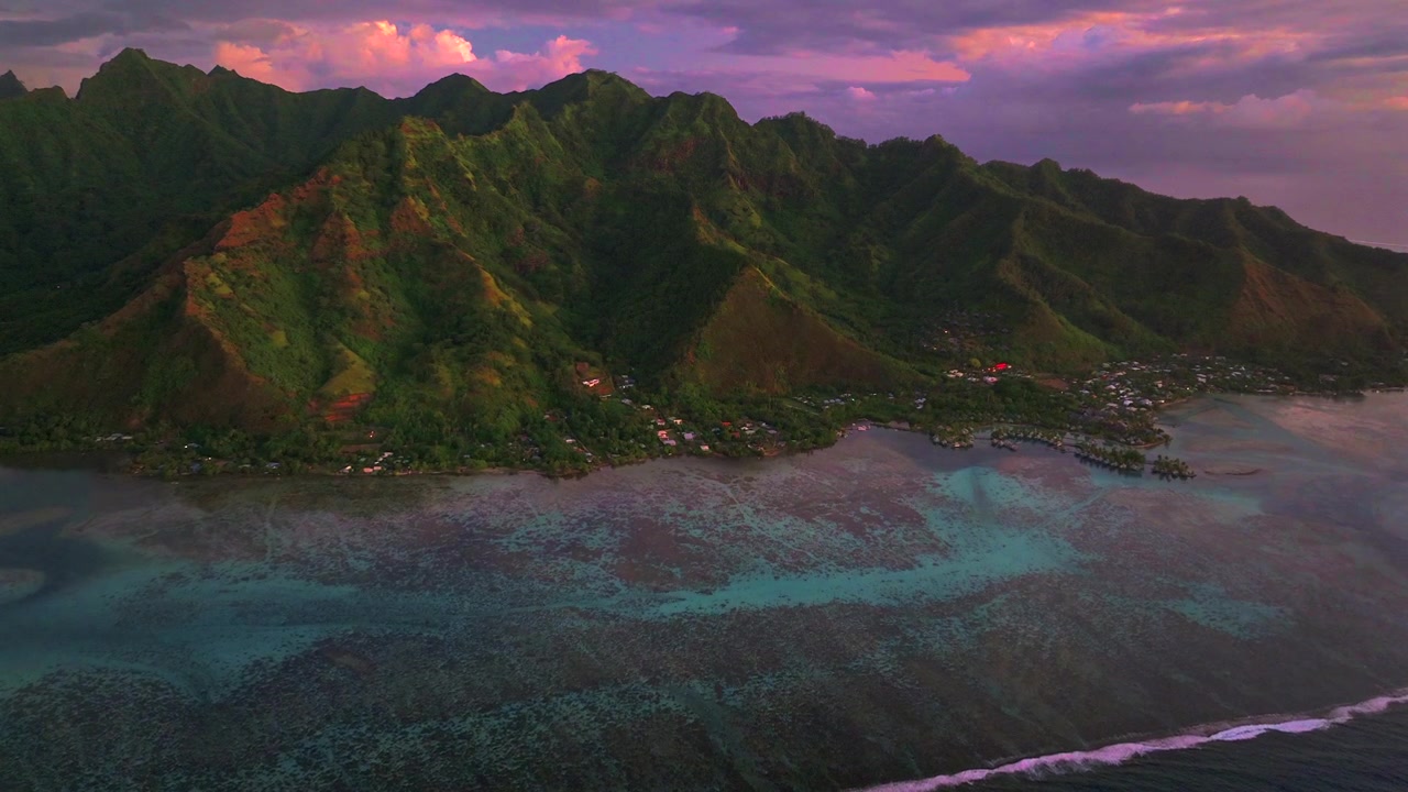 Deep purple pink sunset bungalows Moorea island Cooks Opunohu bay French Polynesia aerial drone blue lagoon coral reef Mount Mauaroa Tohivea Rotui jagged peaks Haapiti Paopao Pacific Ocean forward