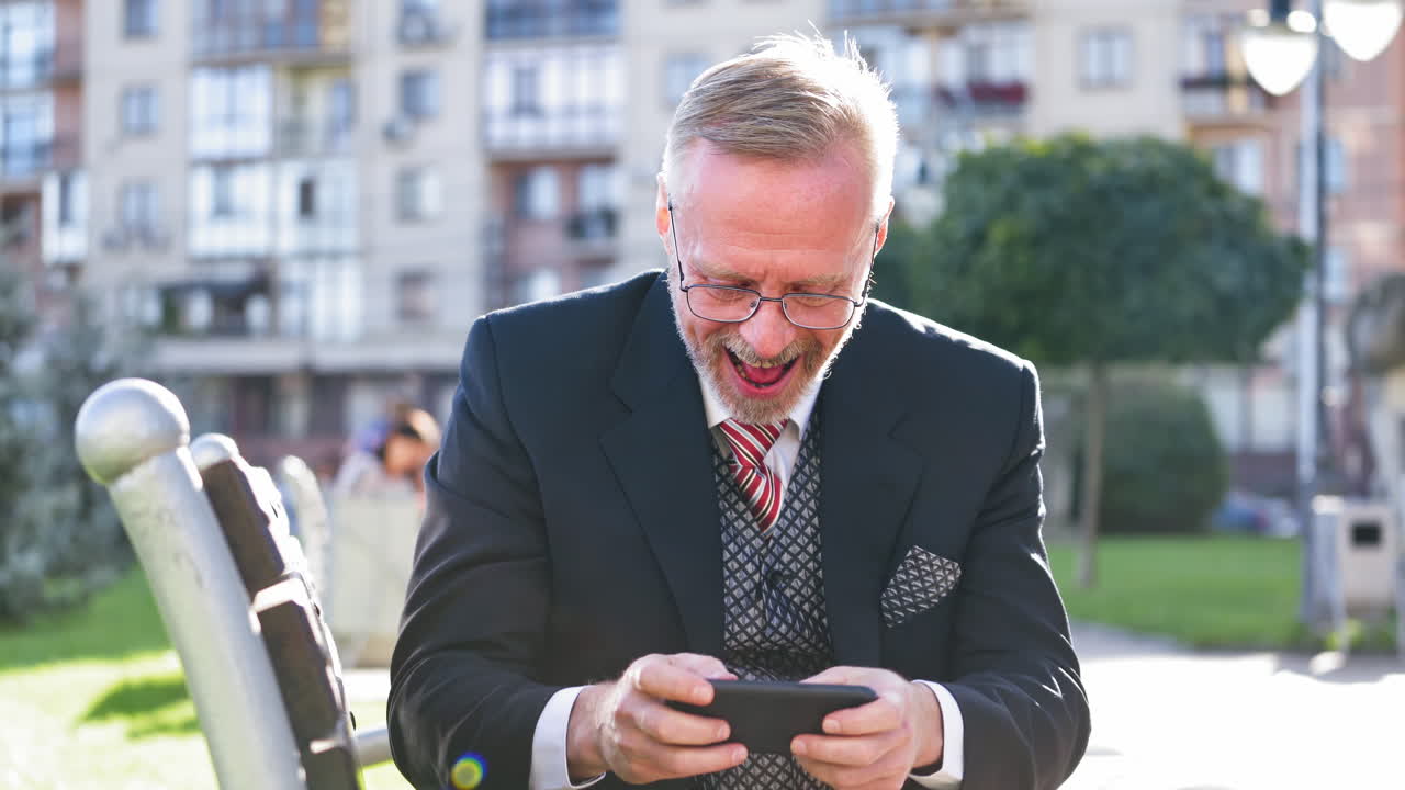 Bearded man playing games. Emotional senior man playing on phone