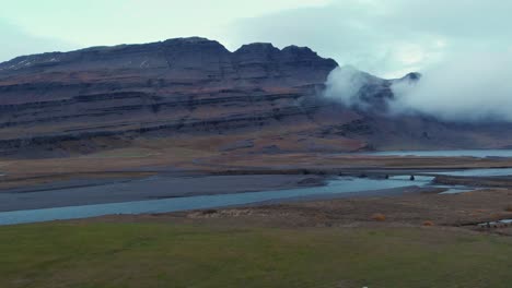 ovejas pastando en un campo de hierba junto a un río debajo de un macizo rocoso, islandia