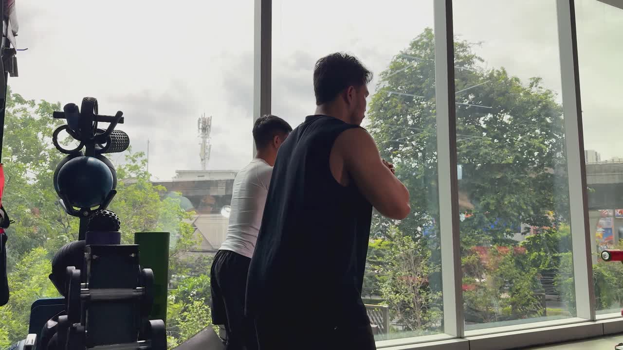 Two men perform synchronized bodyweight squats in a modern gym with city skyline views