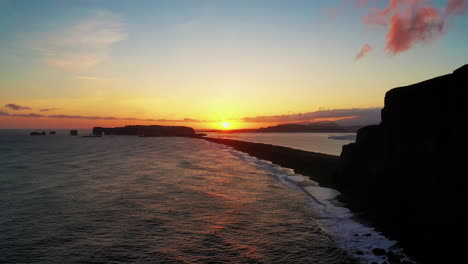 silhouette of reynisdrangar basalt sea stacks in south iceland during sunset - ascending drone shot