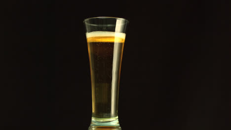 papel quemando y confeti cayendo sobre la cerveza vertiendo en un vaso contra un fondo negro