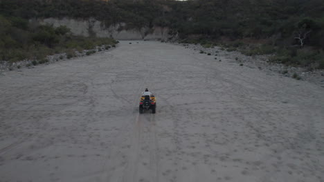 Drone-following-a-man-riding-a-motorcycle-in-a-dusty-road-in-Los-Cabos,-Mexico