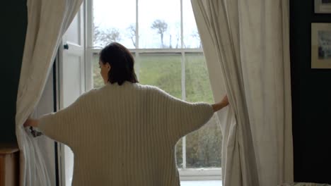 woman opening window curtains