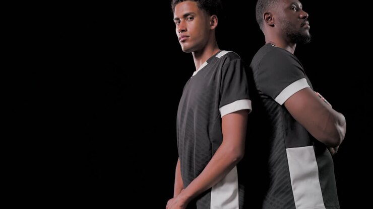 Standing two soccer players posing in studio on turf, wearing black jerseys, resting foot on ball