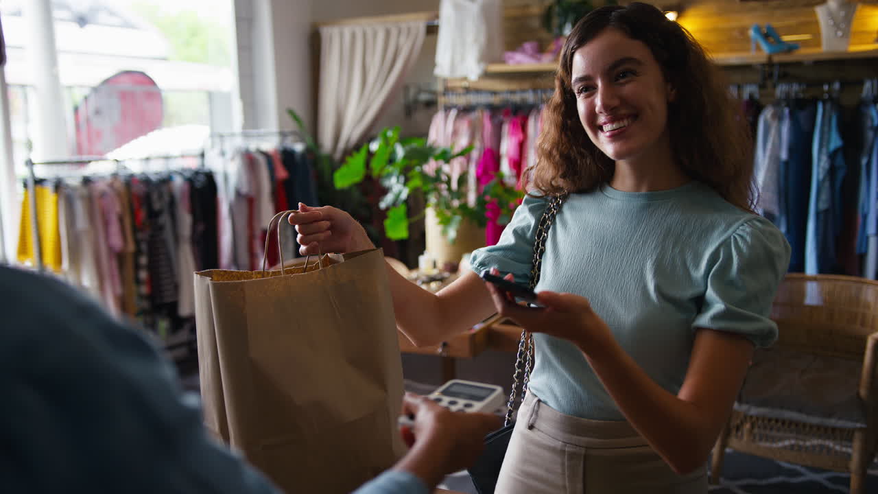Female Customer In Fashion Store Paying For Clothes With Contactless Mobile Phone Payment App