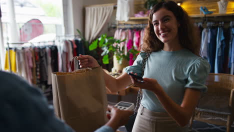 female customer in fashion store paying for clothes with contactless mobile phone payment app