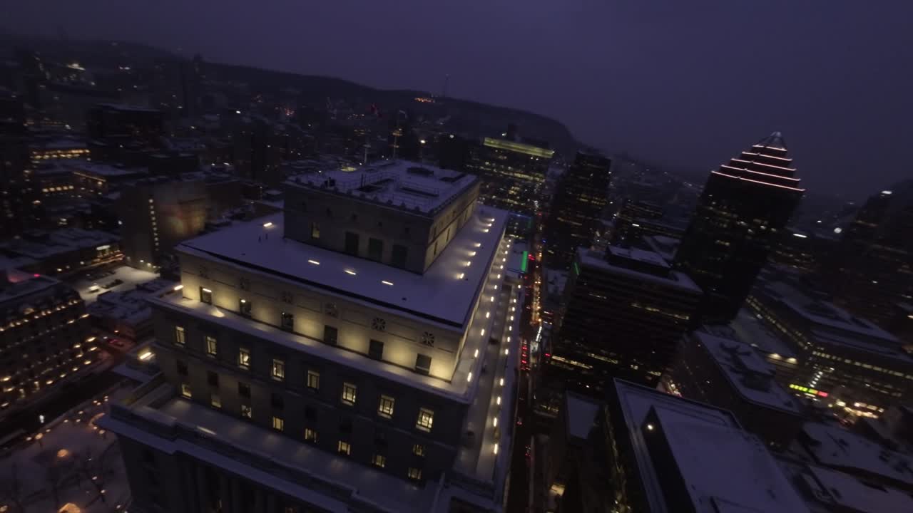 FPV drone flies above snowy roof of Sun Life Building, breathtaking night views of Square Dorchester and Montreal Downtown in winter.