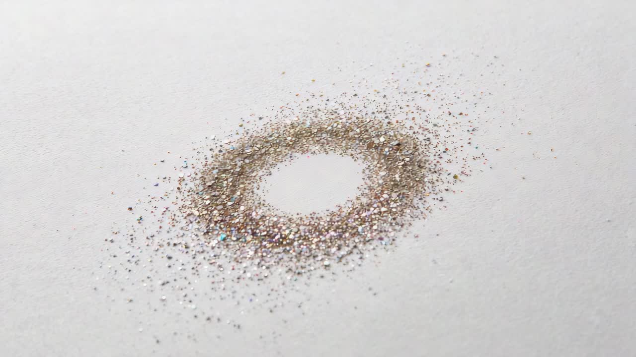 Shifting metallic glitter ring spreading slightly on white sheet, time passing causing dispersion